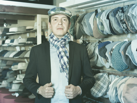 Portrait of positive cheerful young male try on beret at the shopping mallの写真素材