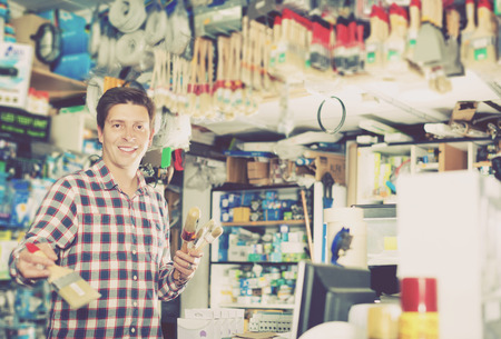 Smiling male standing near the counter and selling brushes for repair and pantingの写真素材