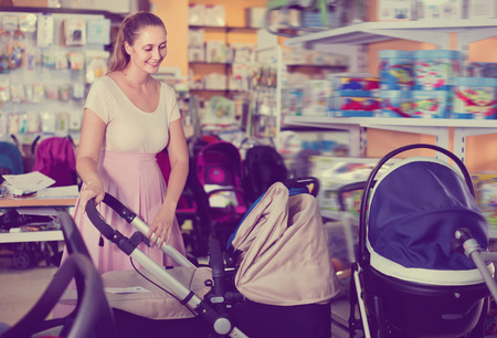 Cheerful smiling pregnant woman buying baby stroller in kids mallの写真素材