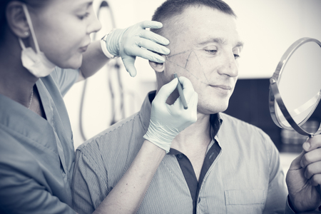 Female specialist is marking zone on face of client in estetic clinic.の写真素材