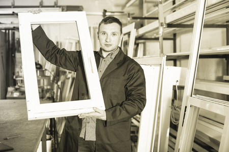 Positive smiling efficient professional  labour with finished PVC profiles and windows at factoryの写真素材