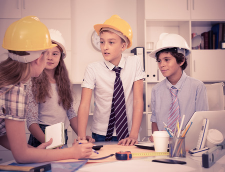 Teens in color helmet engineers discussing draft at the tableの写真素材