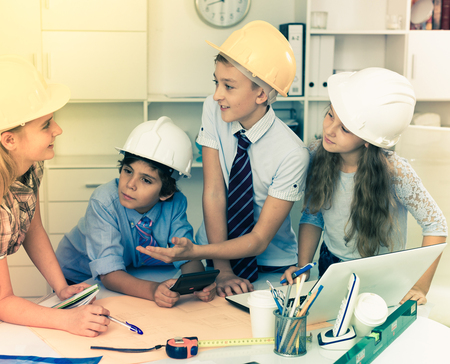 Boys and girls architects with plan near notebook in the officeの写真素材