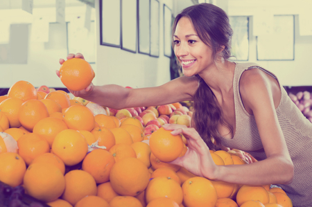smiling american female customer picking oranges on fruit marketの写真素材