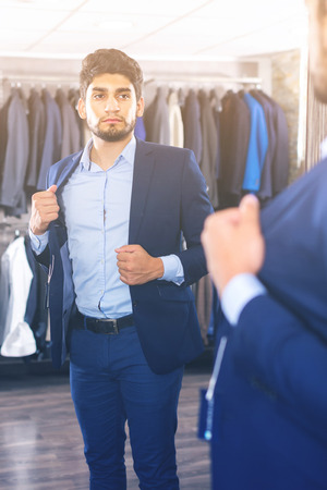 Man 25-33 years old is trying on jacket in front of the mirror in shop.の写真素材