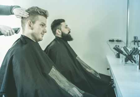 Young positive smiling efficient clients having their hair cut by hairdressers at salonの写真素材