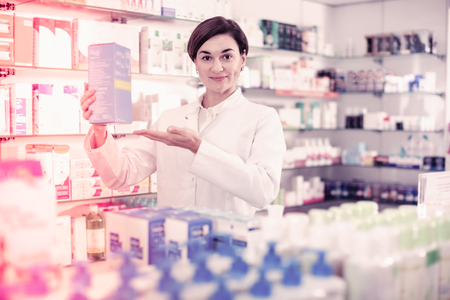 Young cheerful  female pharmacist suggesting useful body care products in pharmacyの写真素材