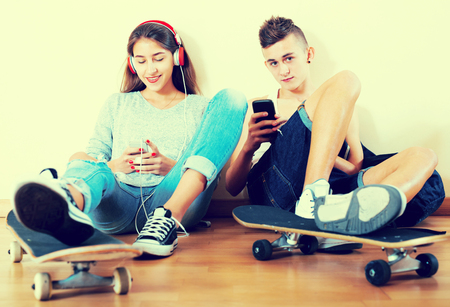 Boy and his smiling girlfriend with smartphones at homeの写真素材
