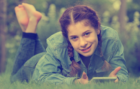 smiling young germany  female using digital tablet while lying in outdoorsの写真素材