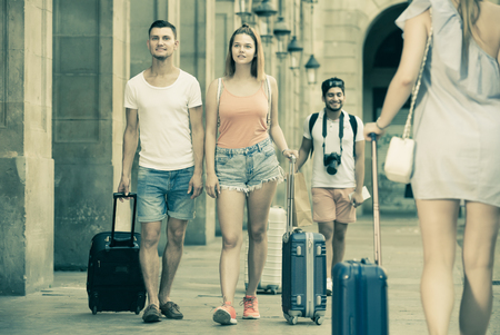 Happy man and woman in shorts with luggage walking through city streetの写真素材