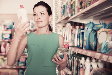 Portrait of glad adult woman choosing dishwashing liquid at the supermarketの写真素材