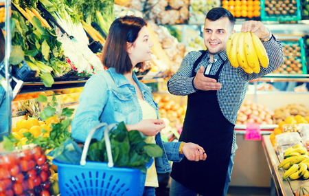 Smiling male seller assisting customer to buy fruit and vegetables in grocery shopの写真素材
