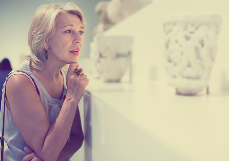 Positive mature woman visitor in the historical museum looking at expositionの写真素材