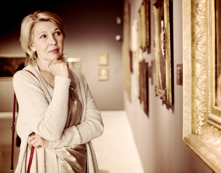 Mature woman standing in art museum near the painting in baguetteの写真素材