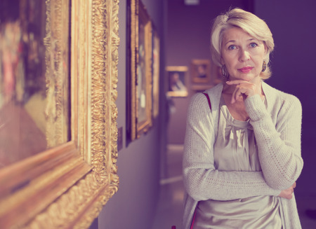 Mature woman standing in art museum near the painting in baguetteの写真素材