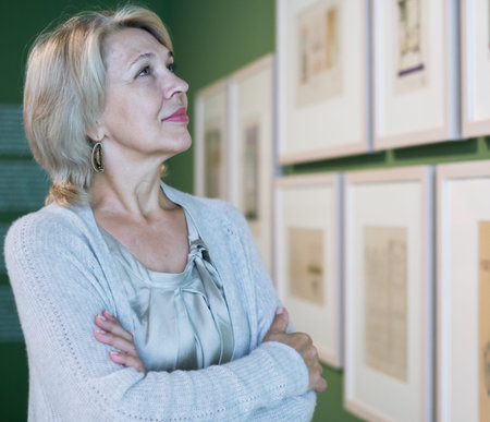 Mature woman standing in art museum near the painting in baguette
