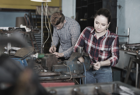 Glad cheerful positive  girl worker is standing near vise equipment in workshop.の写真素材