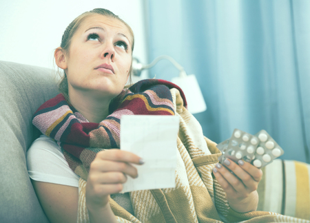 Sick woman lying at home on cozy sofa with plaid and reading recipeの写真素材
