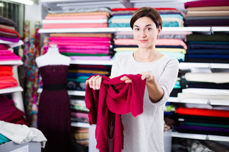 Young female shopper examining fabric quality for dress at drapery shopの写真素材