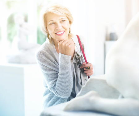 Portrait of positive mature woman visitor near sculpture in the historical museumの写真素材