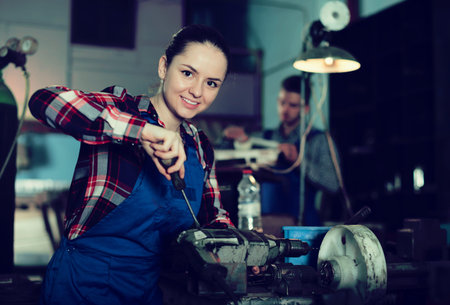 young female who is repairing drill on her workplace in workshop.