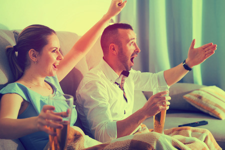 Man is watching football with wife in time resting on sofa at home.の写真素材