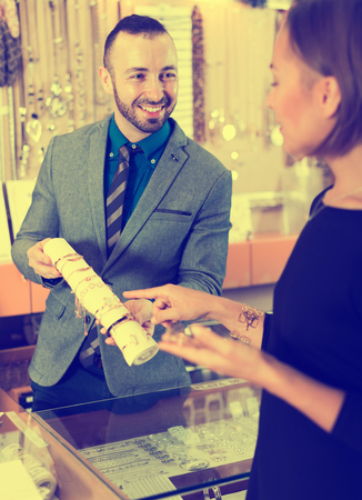 Adult man seller offering bracelets for woman in the jewelry storeの写真素材
