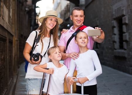 Happy tourist family of four strolling on city streets and taking selfieの写真素材
