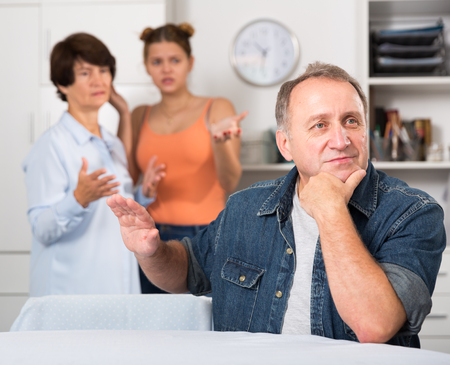 Adult man is upseting and his wife with daughter are sympathying with her at home.の写真素材