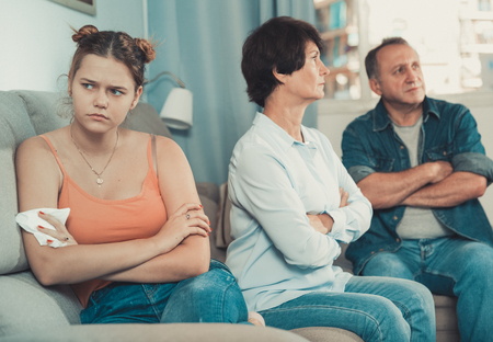 Adult couple is carefully talking with a sad daughter on sofa at home.の写真素材