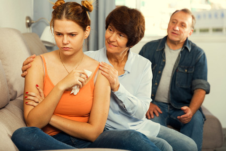 Parents are comforting the upset adult daughter on sofa at home.の写真素材