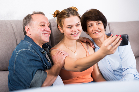 Marrieds with their adult daughter are takinf selfie together on sofa indoor.の写真素材