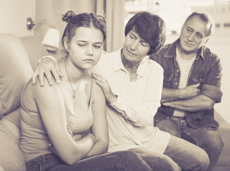 Parents are comforting the upset adult daughter on sofa at home.の写真素材