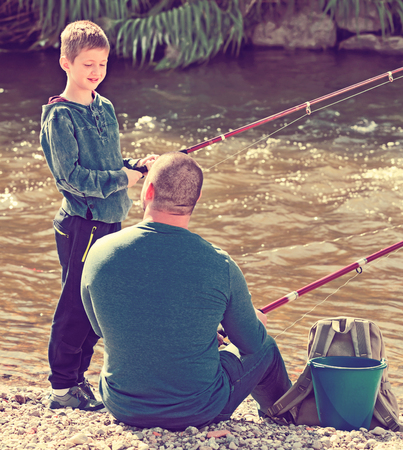 Portrait of happy  laughing father and cute son fishing with rods in summer dayの写真素材