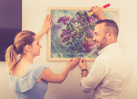 Man is hanging the picture on the wall together with his wife at home.の写真素材