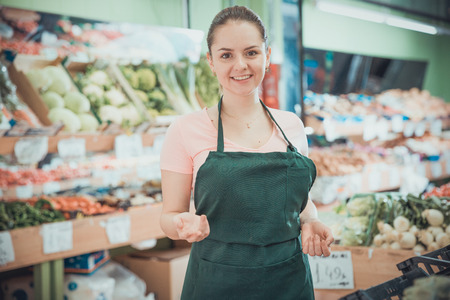 Positive female grocery worker welcoming to vegetable storeの写真素材