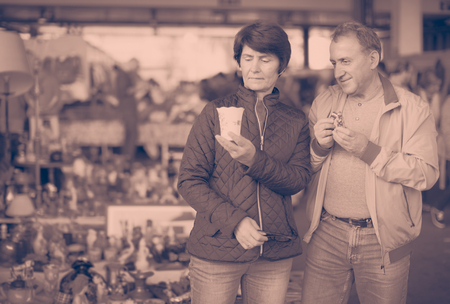 Positive mature couple looking vintage souvenirs at sale on marketの写真素材