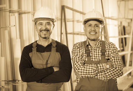 Two positive specialists in helmets and workwear posing at workshopの写真素材