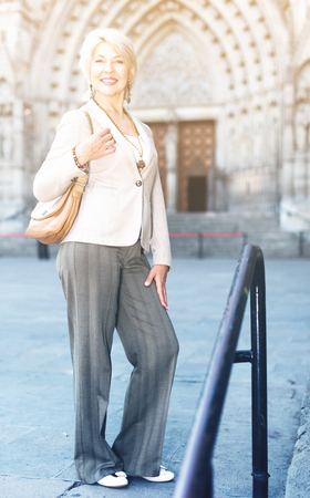 Cheerful mature female is walking in classic jacket on the street outdoor.の写真素材