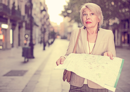 Elegant adult woman is posing with map in time walking on the street of old city.の写真素材