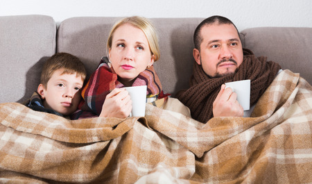 Ill family wrapping in blanket on couch at home drinking hot teaの写真素材