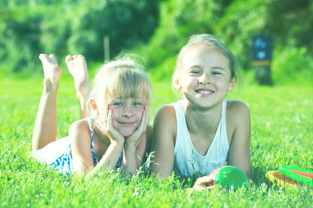 Two happy little girls laying on grass on sunny summer dayの写真素材