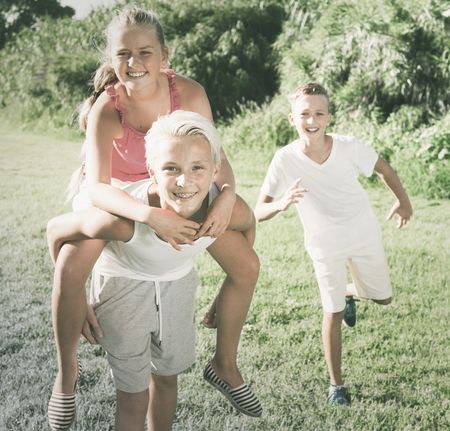 Cheerful girl with two friends having fun together running on summer parkの写真素材