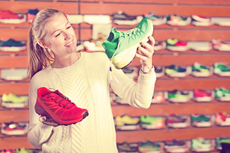 Young slender girl in a sports shop chooses her a clothes and shoes for trainingの写真素材
