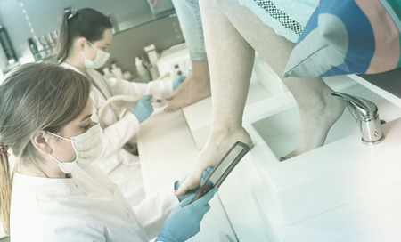 Close-up nail technicians giving pedicure to female clients at nail salonの写真素材