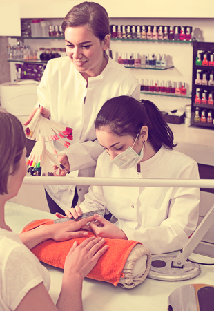 happy european manicurists choosing color of nail polish with client in nail salonの写真素材