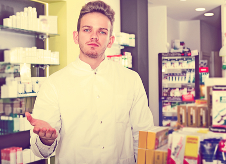 Young man pharmacist wearing uniform and working in pharmaceutical shopの写真素材