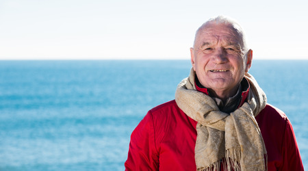 Senior man taking walk by sea on sunny chilly dayの写真素材