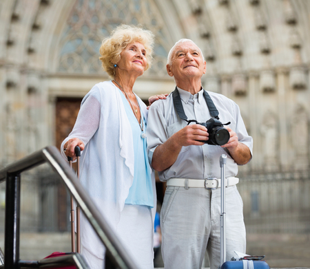 Glad cheerful positive senior couple admiring city sights during joint vacation, making photo with cameraの写真素材