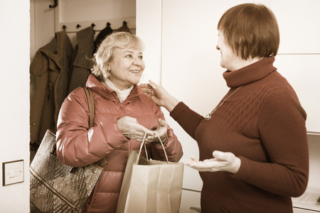 Positive old woman saying goodbye to friend female in jacket indoorsの写真素材